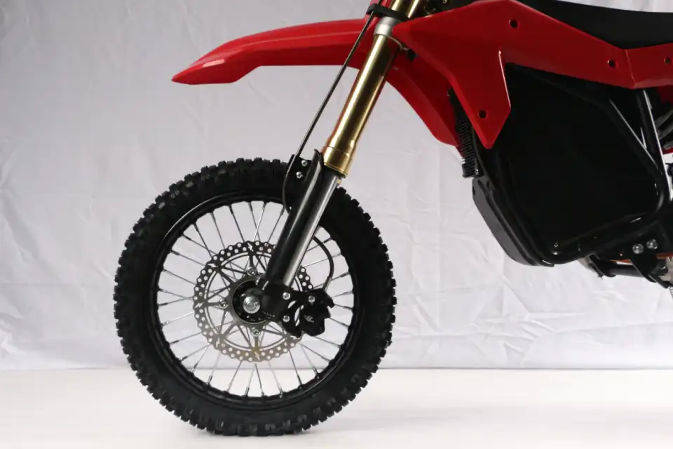 Front wheel and suspension of a red dirt bike, featuring a knobby tire, disc brake, and gold fork.]